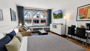 A hotel room with a bed, sofa, desk, and a view of buildings through large windows. - Very Cute Studio Next To Ski Slope WiFi Village (Snowshoe)
