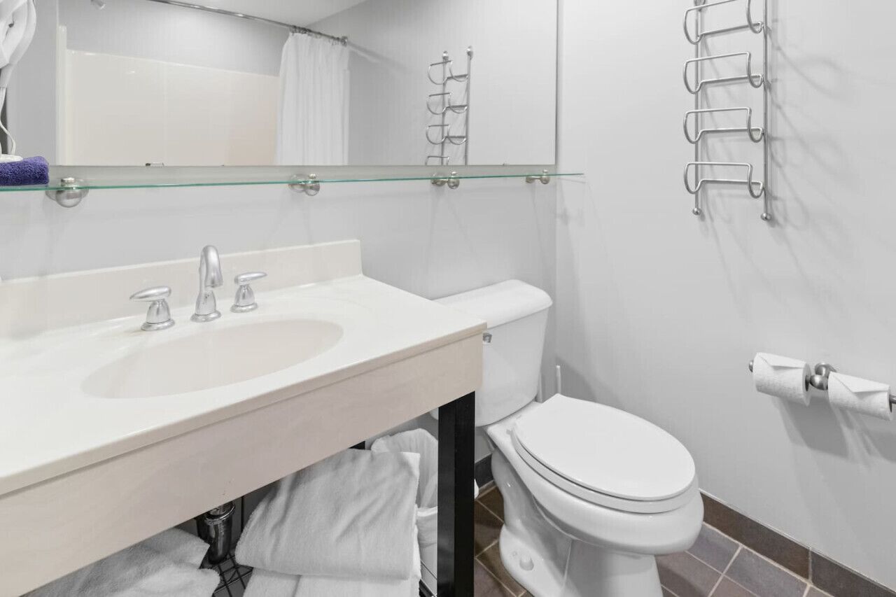 A modern bathroom with a glass shelf above the sink, a toilet, and a towel rack on the wall.