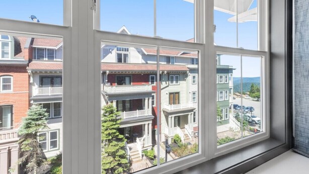 A view through a window with multiple panes, displaying a row of multi-story residential buildings with balconies and a clear sky. - Very Cute Studio Next To Ski Slope WiFi Village (Snowshoe)