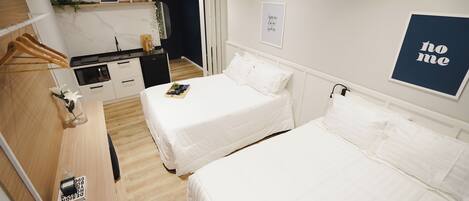 A hotel room with two beds, a kitchenette, and a 'home' sign on the wall.