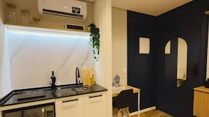 Eine moderne Küche mit weißen Schränken, einer schwarzen Arbeitsplatte und einer eingebauten Mikrowelle. Ein Holztisch mit einem Stuhl, ein Topfpflanze und eine kleine Statue an der Wand sind ebenfalls vorhanden.