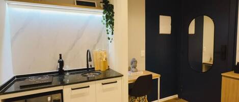A modern kitchen with white cabinets, a black countertop, and a built-in microwave. There is a wooden dining table with a chair, a potted plant, and a small statue on the wall.