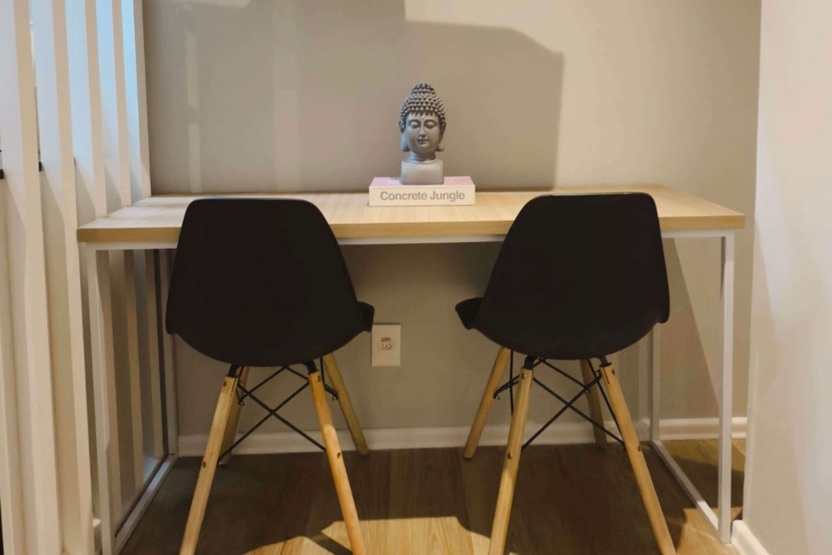 A desk with a bust sculpture labeled "Concrete Jungle" and two black chairs.
