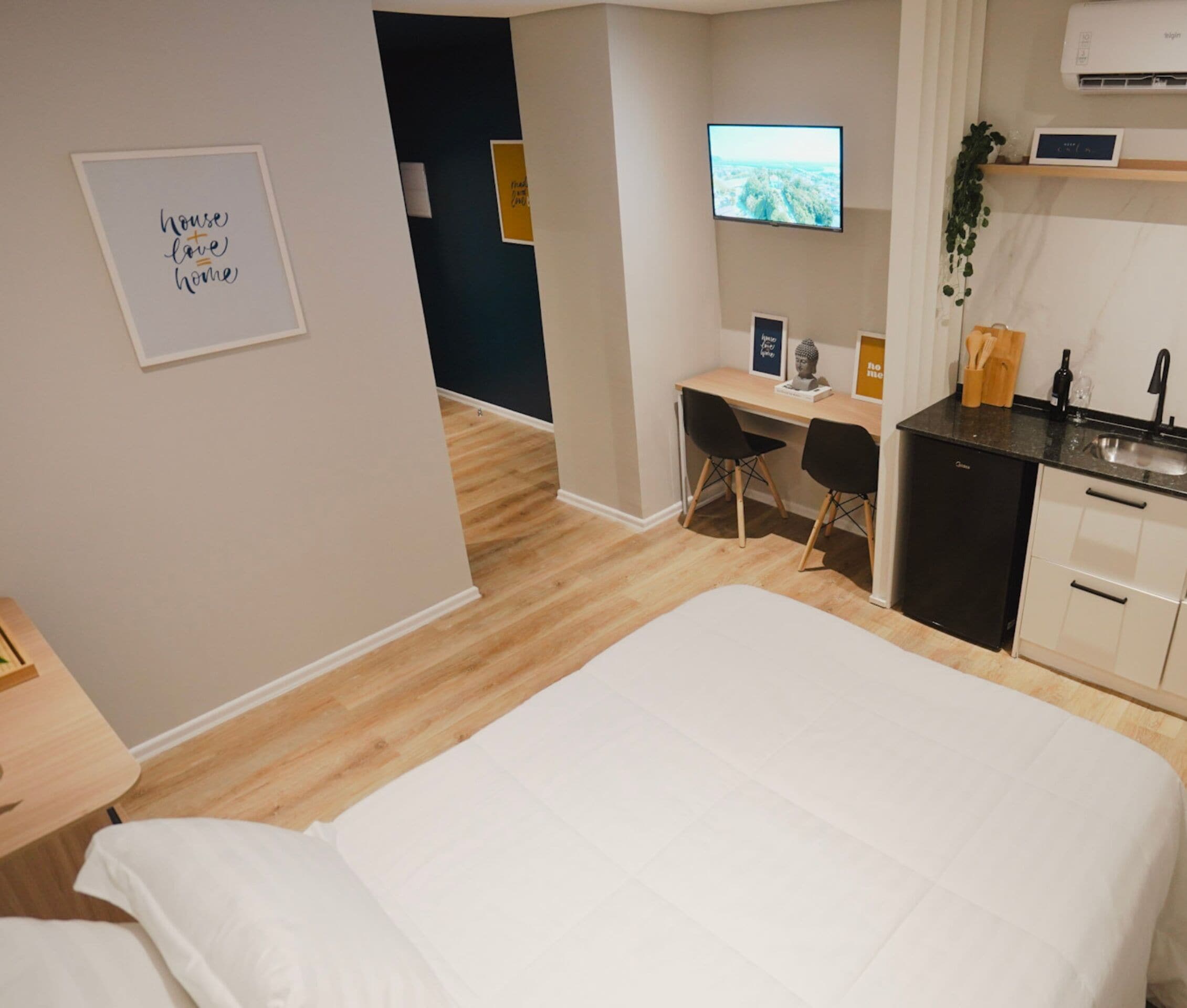 A hotel room with a bed, a desk, a chair, a TV, a small kitchen area, and a bathroom.
