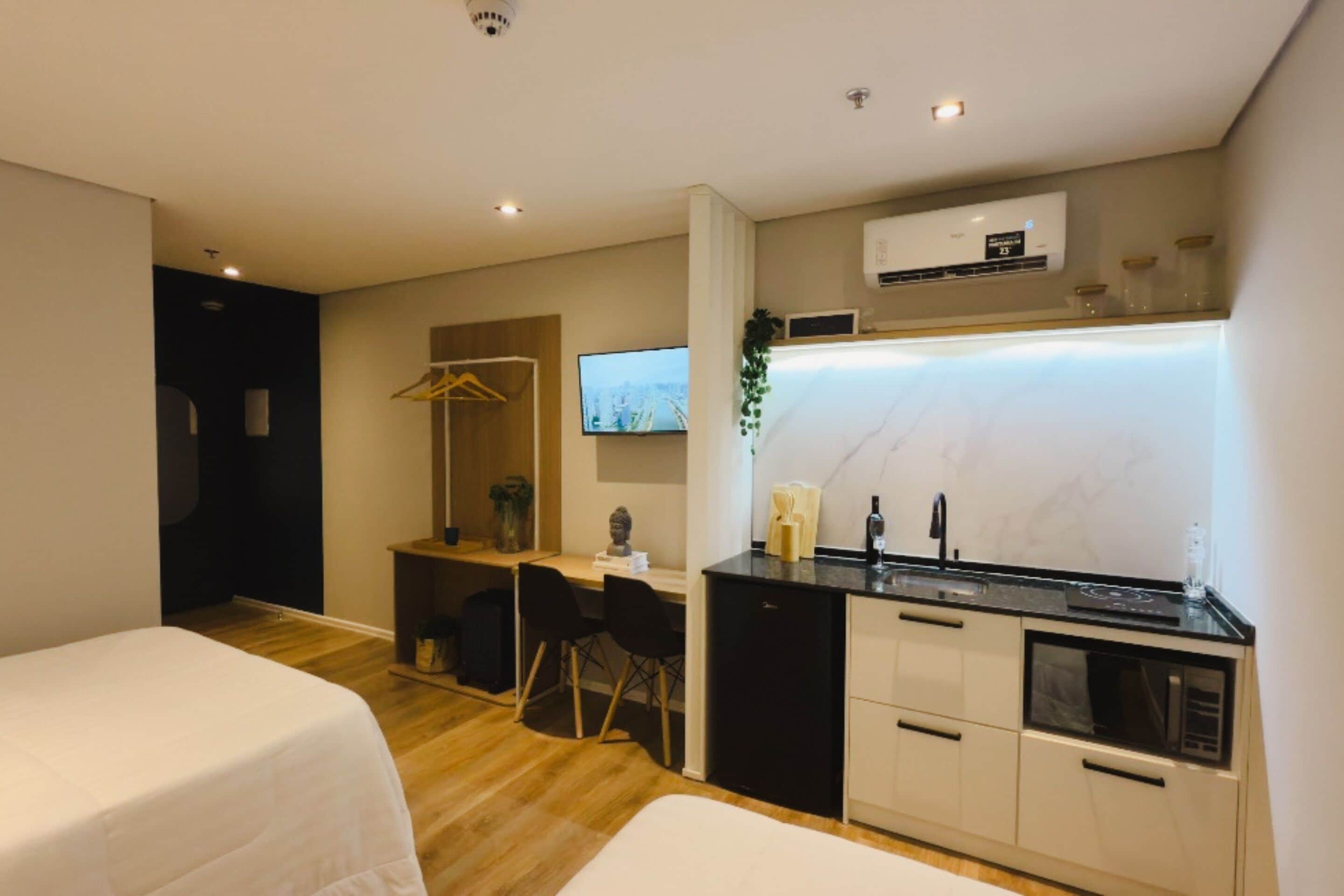 A modern hotel room with a kitchenette, a TV, and a bed.