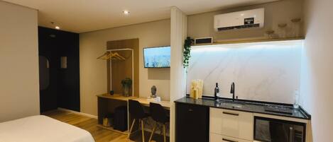 A modern hotel room with a kitchenette, a TV, and a bed.