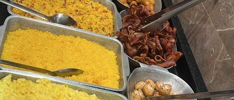 Un bufé con diversos platos, entre ellos huevos revueltos, arroz y diferentes tipos de carne.