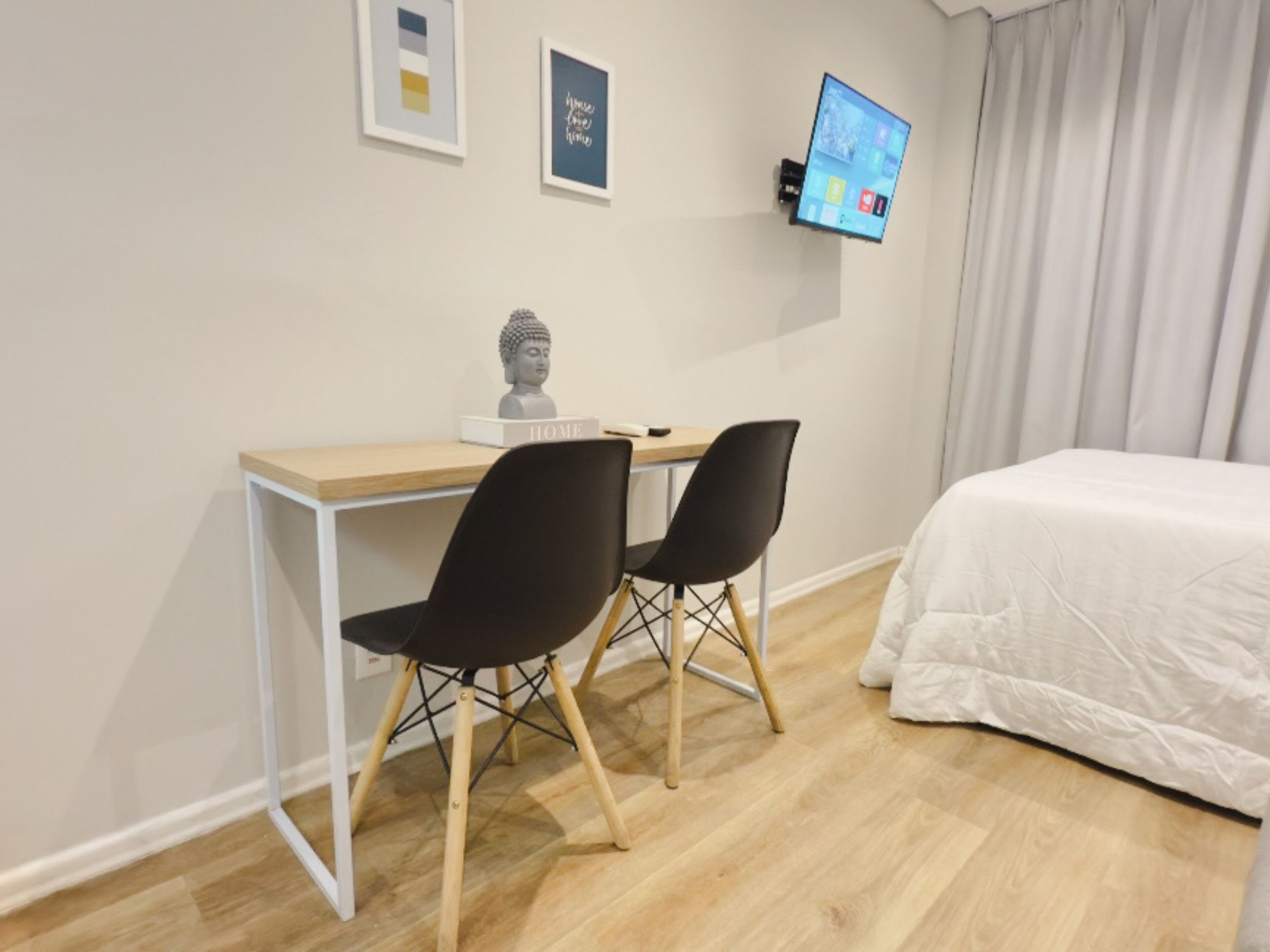 Um quarto com uma cama, uma escrivaninha com duas cadeiras, um busto de Buda e uma televisão fixada na parede.