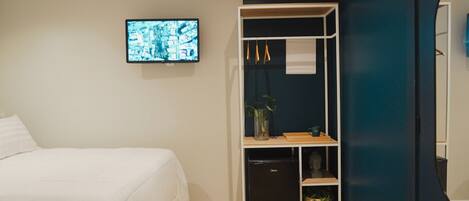 A bedroom with a bed, a TV mounted on the wall, a built-in wardrobe, and a small black refrigerator.