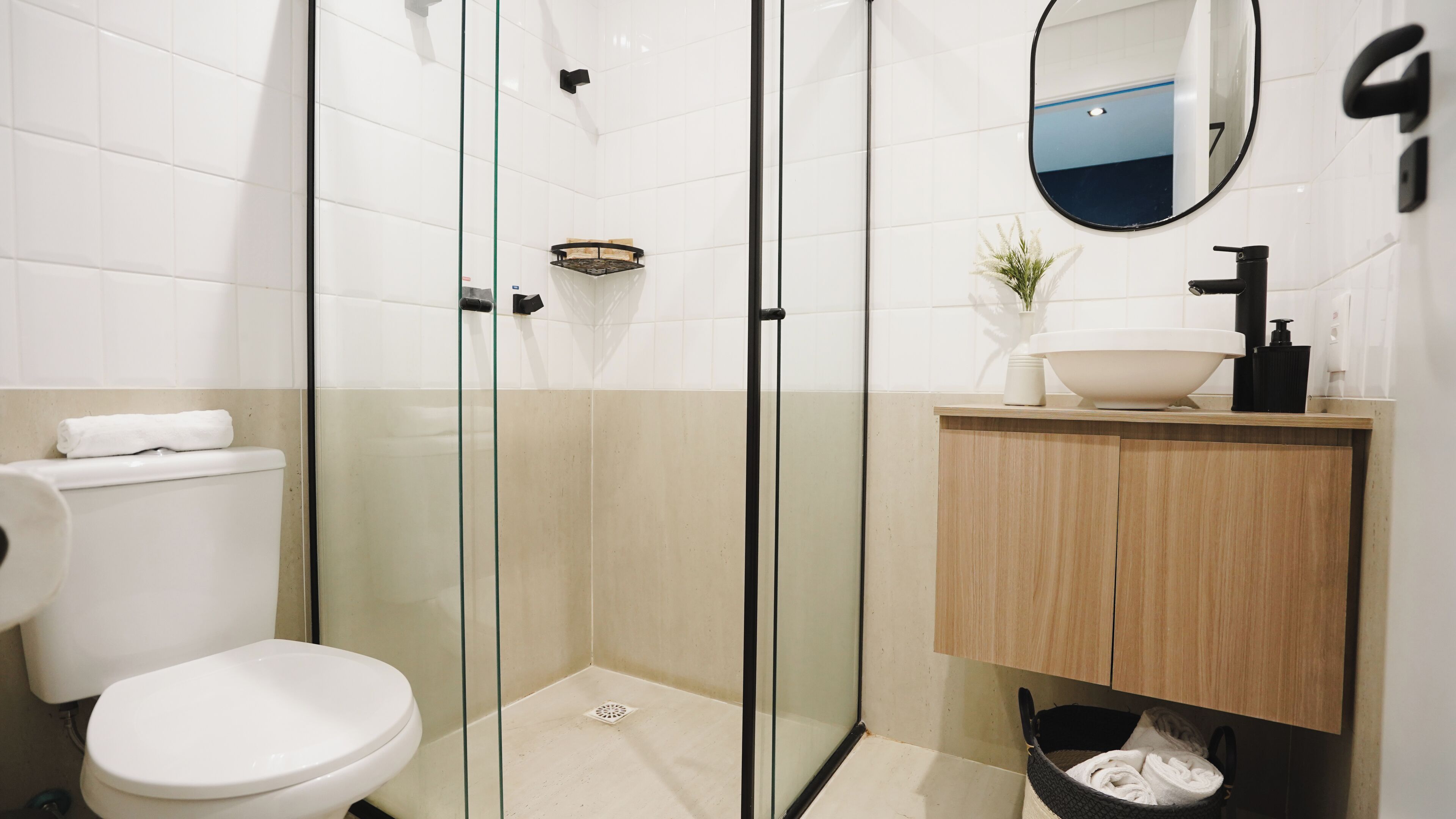 A modern bathroom with a glass-enclosed shower, a toilet, a sink with a wooden cabinet, and a mirror.