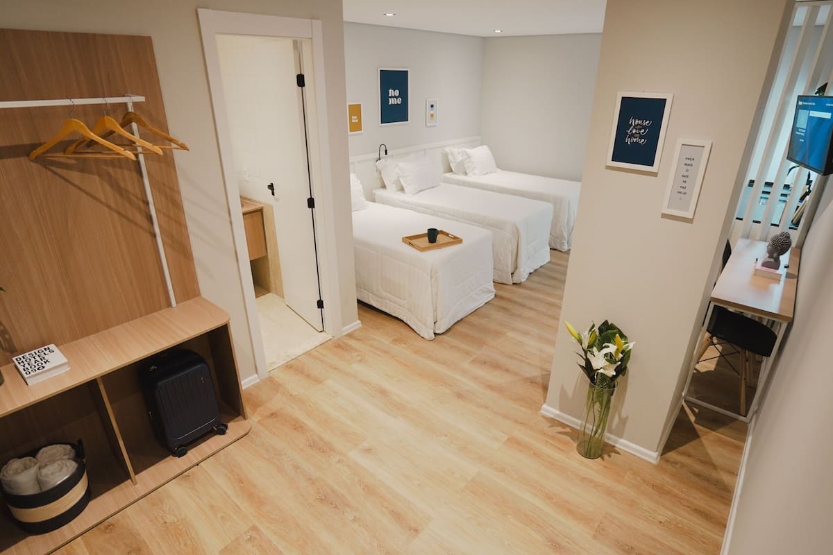 Ein Hotelzimmer mit zwei Betten, einem Holzschrank, einem Schreibtisch mit Computer und einer kleinen Pflanze.