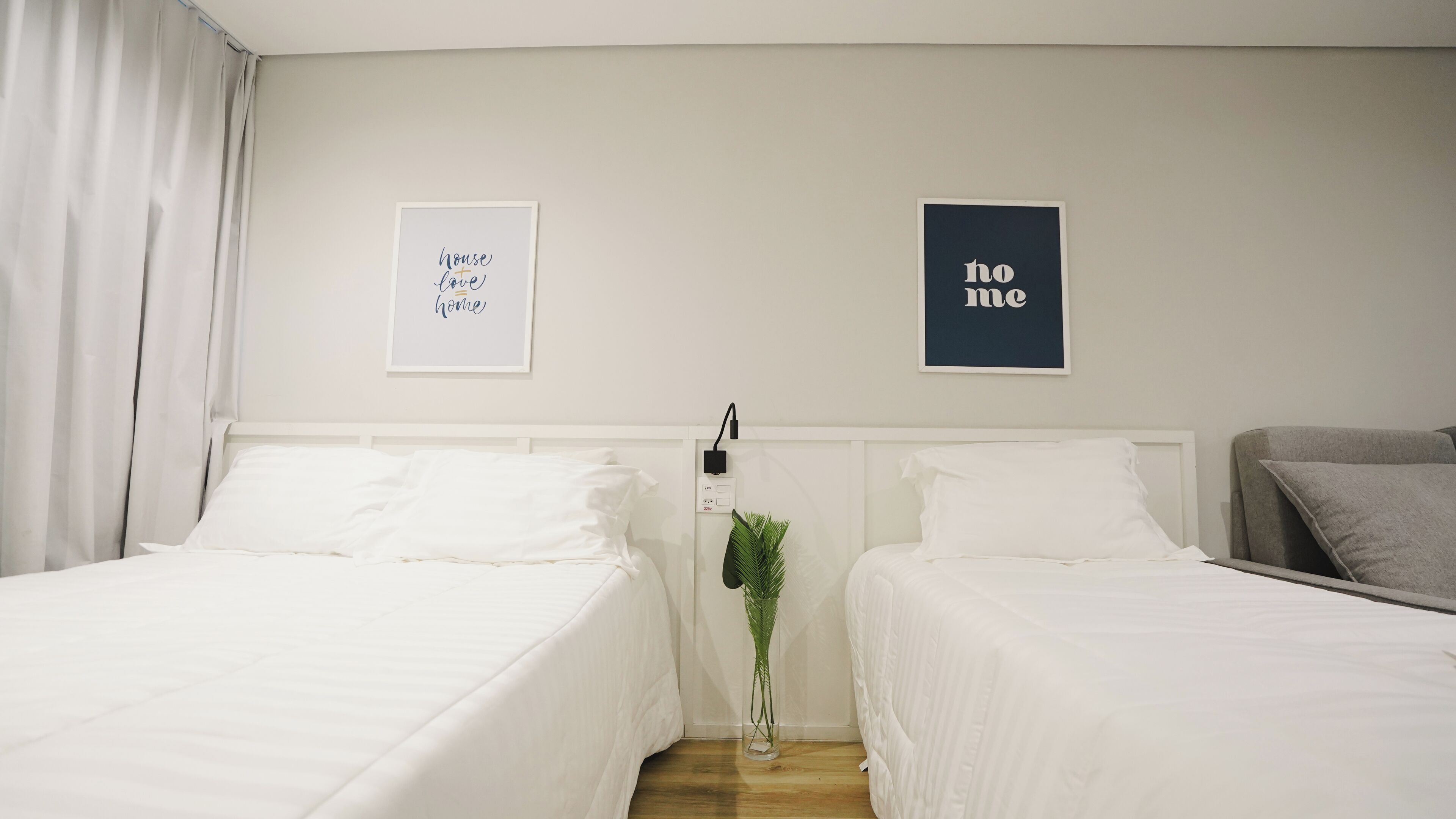 Habitación de hotel con dos camas, una mesita de noche con lámpara y dos cuadros en la pared.