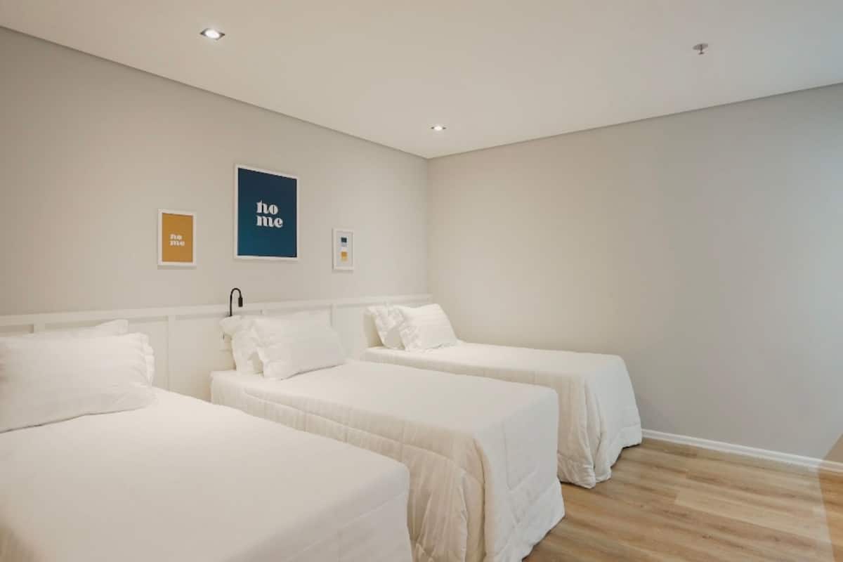 Ein Hotelzimmer mit zwei Einzelbetten, einem weißen Kopfteil und einer Wand mit drei gerahmten Bildern.