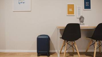 A room with a desk, two black chairs, a blue suitcase, and framed artwork on the wall.