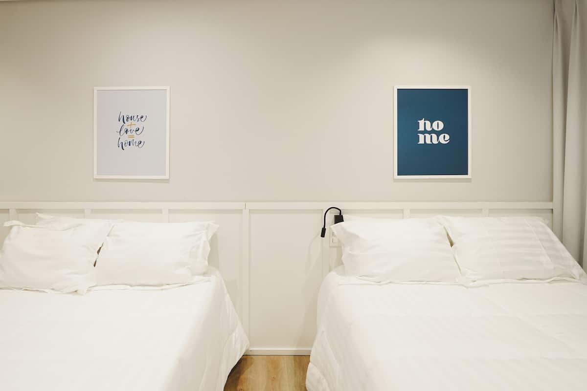 Ein Hotelzimmer mit zwei Betten, einem weißen Kopfteil und zwei gerahmten Bildern an der Wand.