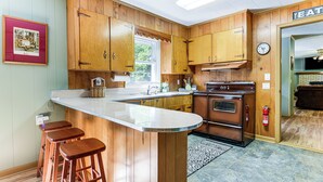 A kitchen with wooden cabinets, a built-in oven, and a bar area with stools. - 6 Mi to Waterrock Knob: 'Serenity Cottage' (Maggie Valley)