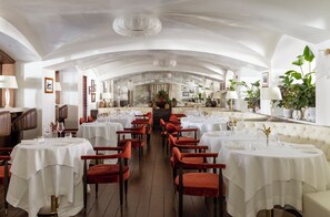 Ein Restaurant mit mehreren runden Tischen, roten Samtstühlen und einer weißen Decke mit einem Kronleuchter.