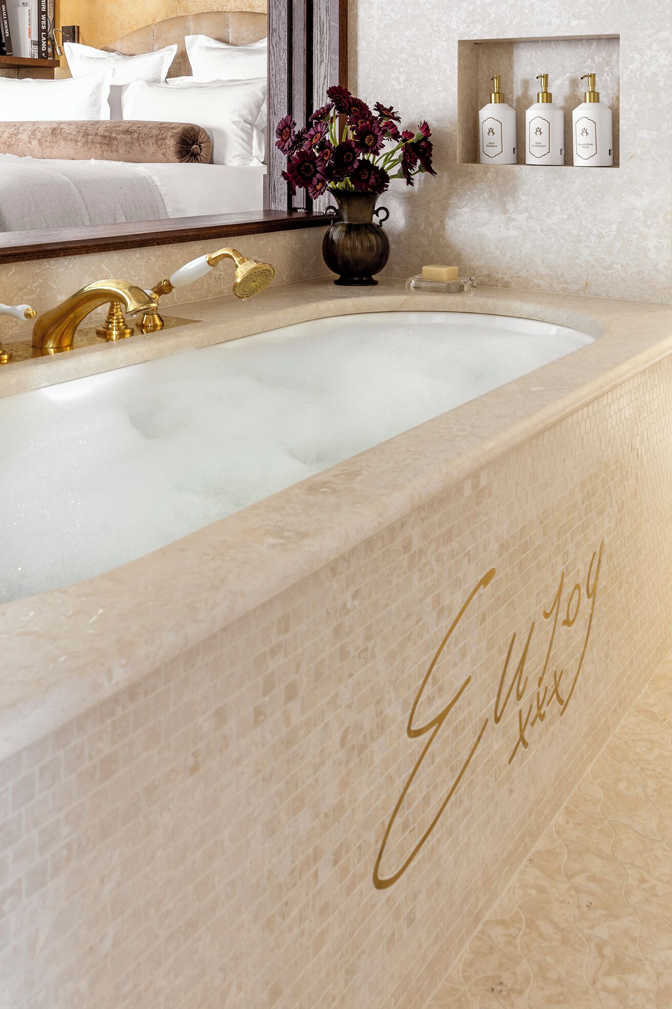 A bathroom with a marble sink, gold fixtures, and a vase of flowers.