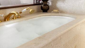 A bathroom with a marble sink, gold fixtures, and a vase of flowers.