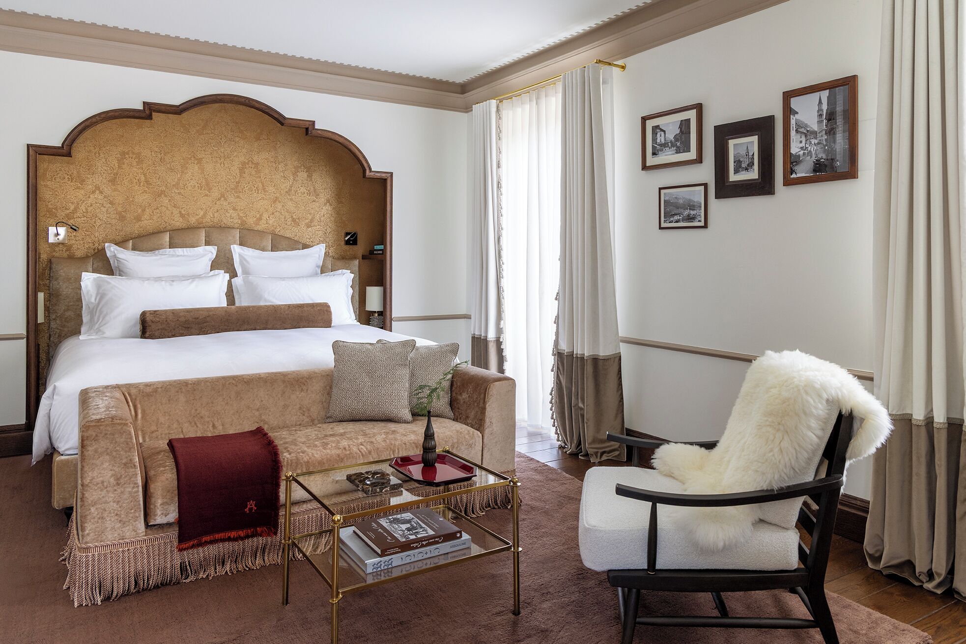 Habitación de hotel con una cama grande, una mesa de centro de cristal con libros, un sillón cómodo y cuadros en la pared.