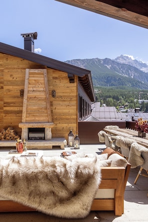 A wooden cabin with a stone fireplace, outdoor seating with fur throws, and a mountain view. - Ancora Cortina (Cortina d'Ampezzo)