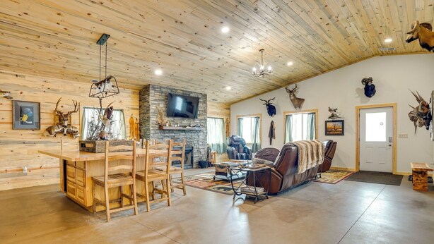 Ein geräumiges Wohnzimmer mit Holzbalkendecke, einem Steinkamin, einem an der Wand montierten Fernseher und verschiedenen Tierkopf-Dekorationen.