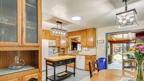 A kitchen with wooden cabinets, a wooden dining table, and a vase with flowers. - Burney Cottage w/ Game Room: Walk to Town! (Burney)