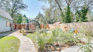 A stone pathway leading to a wooden deck with a covered seating area, surrounded by a wooden fence and various plants. - Burney Cottage w/ Game Room: Walk to Town! (Burney)