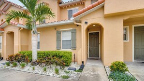 A two-story house with a beige exterior, a palm tree, and a small garden with various plants. - 4 Mi to Disney! Family Townhome w/ Pool Access (Kissimmee)