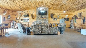 Interior de una cabaña de troncos con chimenea de piedra, televisor montado y diversas jarras de animales en las paredes.