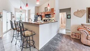 Een ruime keuken met een centraal eiland, hanglampen en een bar met krukken.