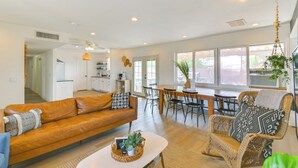 A spacious living area with a sofa, dining table, and wicker chairs. A kitchen is visible in the background. - Water Views & Close to Beach: Home in Lake Havasu (Lake Havasu City)