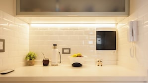 A kitchen with white tiles, a coffee maker, a fruit bowl, a small plant, and a phone on the counter.