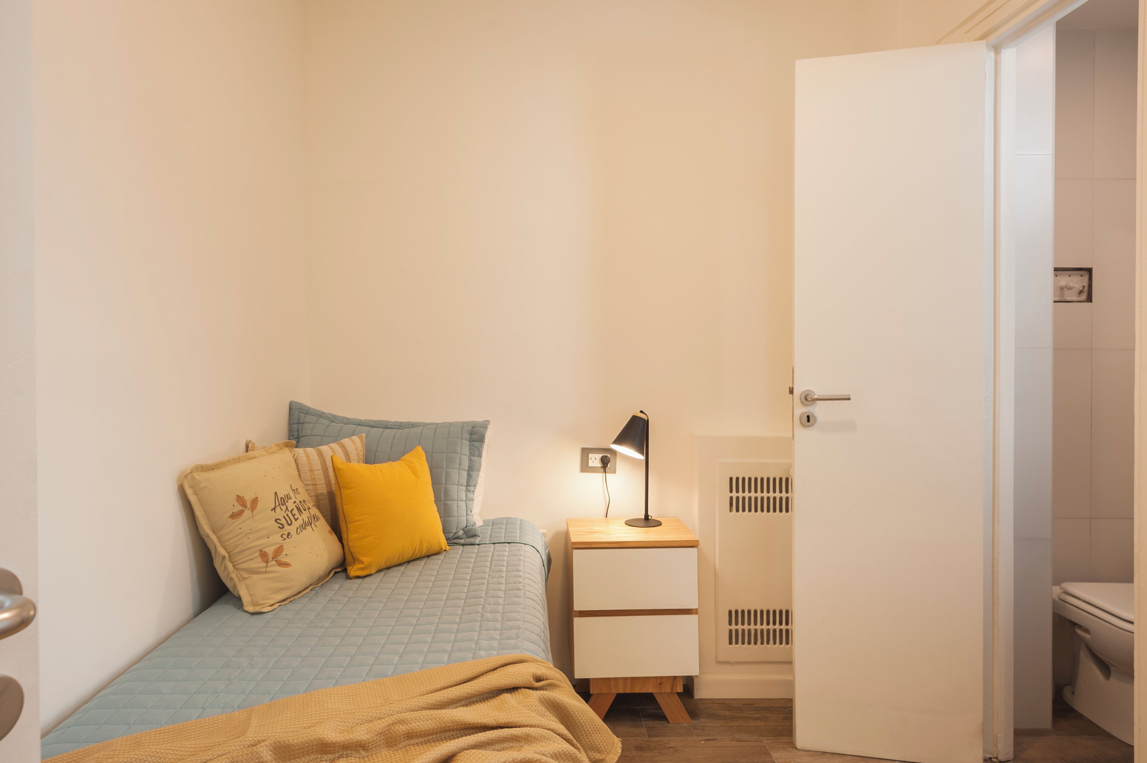 Una camera da letto con un letto, un comodino, una lampada e una porta che dà su un bagno.