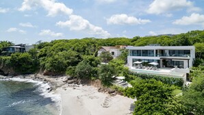 Una propiedad costera con una casa moderna de dos pisos, piscina privada y exuberante vegetación.