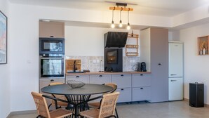 Cuina moderna amb electrodomèstics integrats, zona de dinar amb cadires de vimetla i un refrigerador petit.