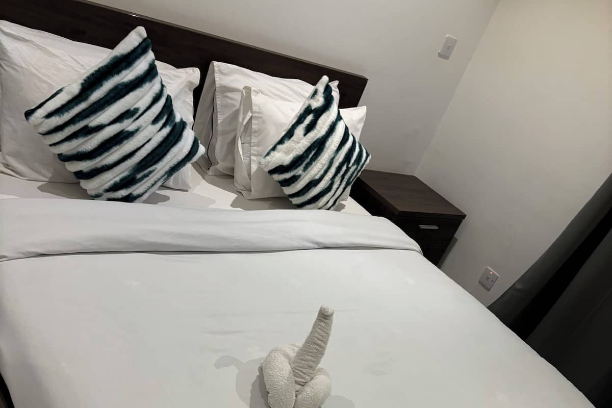 Un lit bien fait, avec du linge de lit blanc et des oreillers à rayures, une tête de lit en bois et une petite table de chevet avec une lampe.