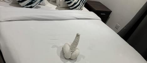 Een net opgemaakt bed met witte lakens en gestreepte kussens, een houten hoofdbord en een klein nachtkastje met een lamp.