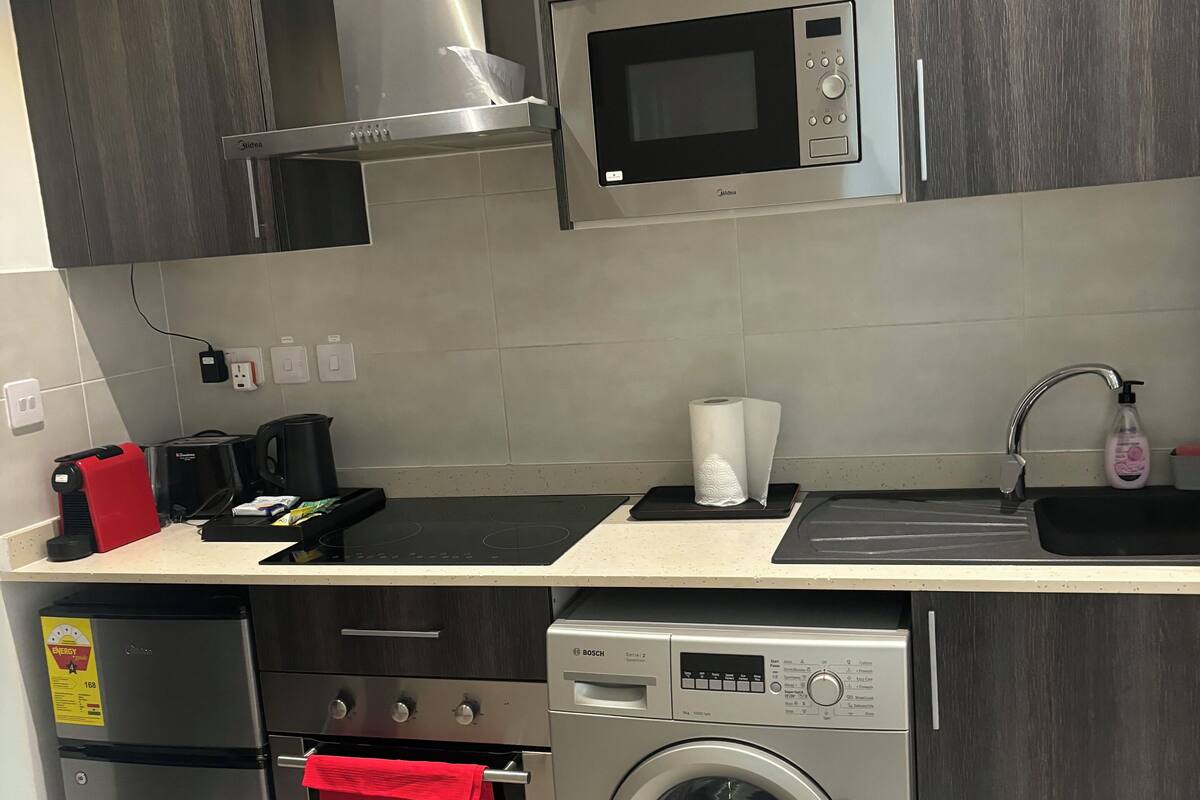 Une cuisine moderne équipée d’un lave-linge Bosch, d’un four à micro-ondes, d’une machine à café et d’une serviette rouge accrochée à la poignée du four.