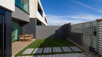 A modern outdoor patio with a dining area, artificial grass, and a grey fence.