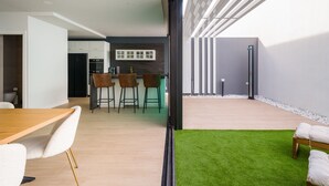 A modern kitchen with white cabinets, a black refrigerator, and a marble backsplash. There are three brown bar stools and a wooden dining table with white chairs. - Sunset Beach Chalet in Pozo Izquierdo Gran Canaria (Santa Lucia)