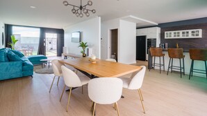 A modern living room with a wooden dining table, white chairs, a teal sofa, and a kitchen area with bar stools. - Sunset Beach Chalet in Pozo Izquierdo Gran Canaria (Santa Lucia)