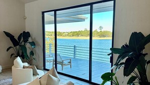 Uma sala de estar ampla com uma grande porta de vidro deslizante que dá para um deck com vista para a água.