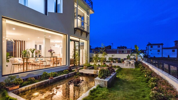 A modern house with a large glass window, a small pond, and a well-maintained garden. - The Field Inn (Dali)