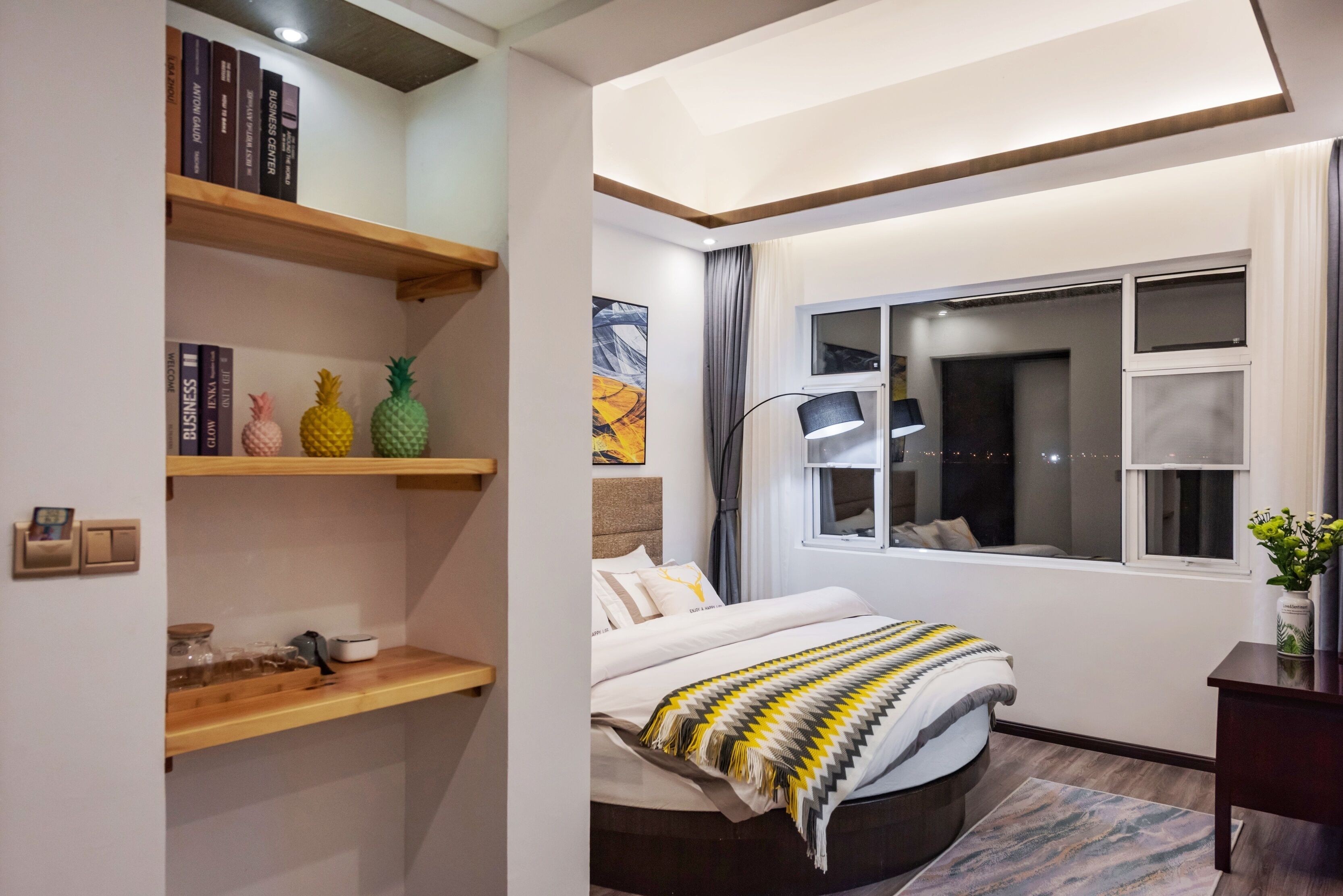 Quarto moderno com cama, prateleiras de madeira, janela e uma pintura.