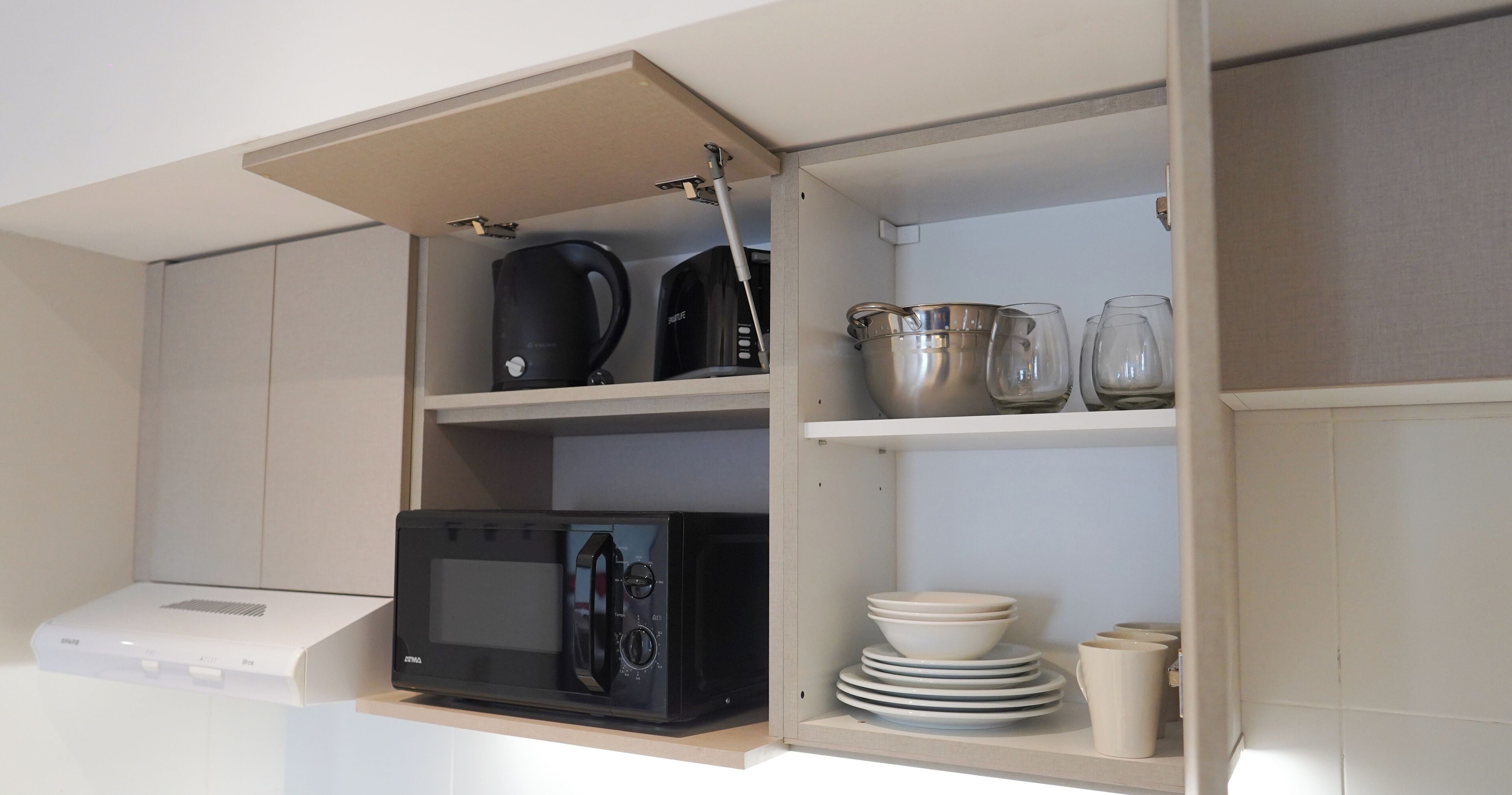 A kitchen with a microwave, kettle, and stacked plates.