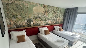Habitación de hotel con tres camas, un gran mural floral en la pared, cabecera roja y vistas al exterior.