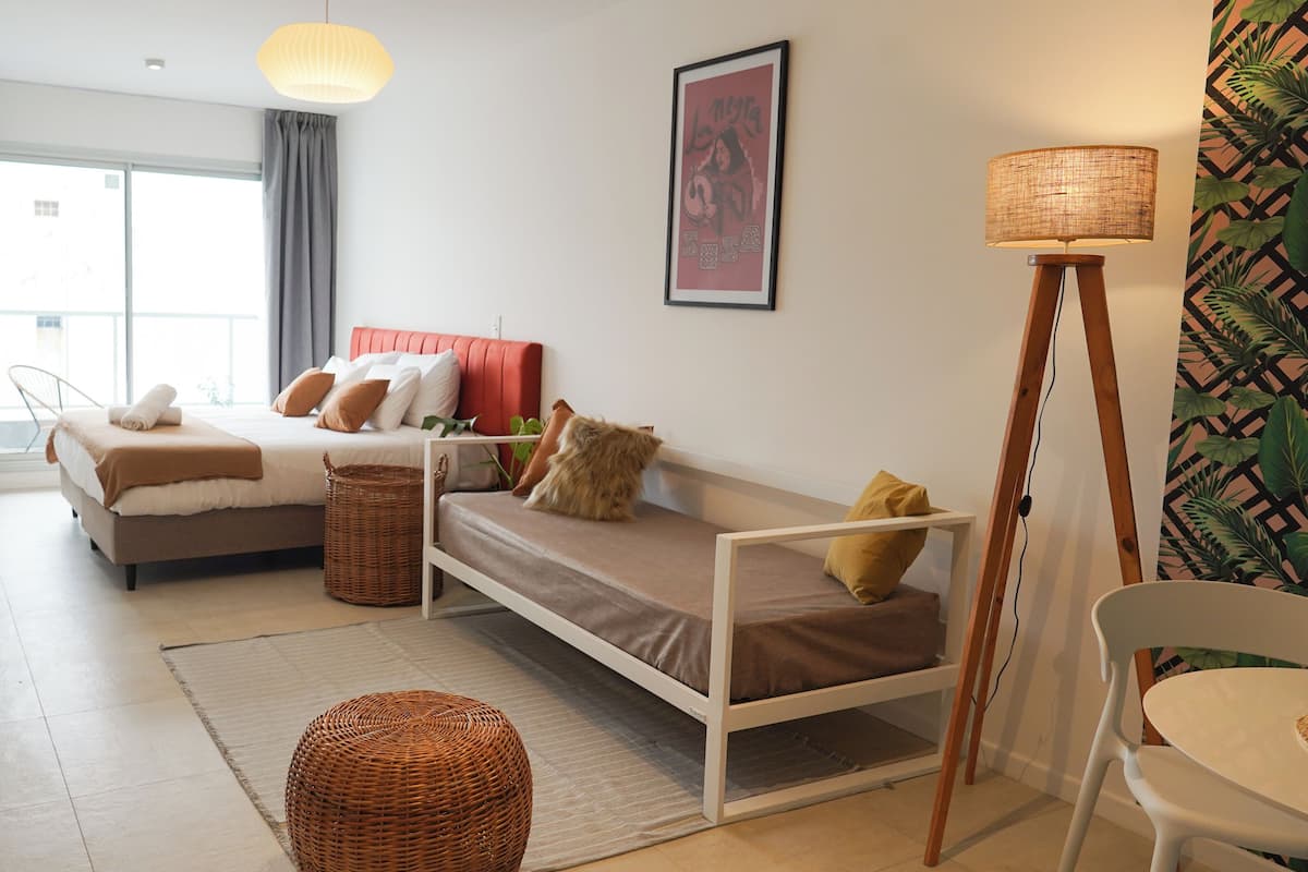 A modern hotel room with a bed, a sofa, a dining table, and a lamp.