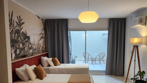 Habitación de hotel con dos camas, un ventanal con cortinas, una lámpara colgante y un aire acondicionado de pared.