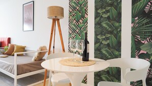 Una habitación con una cama, una mesita redonda con una botella y vasos, una lámpara de pie y una pared con un diseño de hojas.